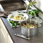 Stainless steel pot on a kitchen counter with food and utensils