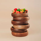 Stack of wooden bowls with colorful fruits on a beige background