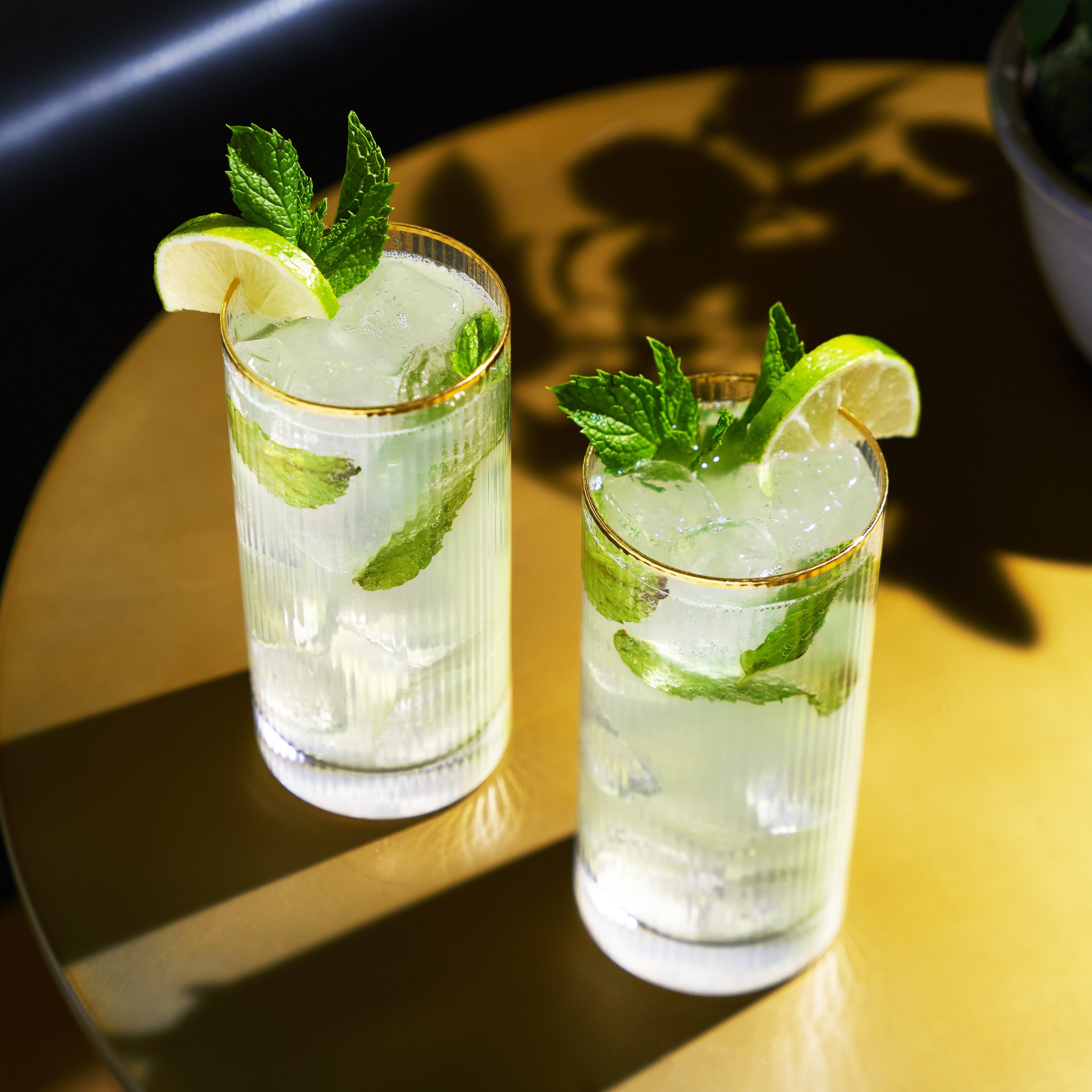 Two glasses of mojito with lime and mint leaves on a reflective surface.