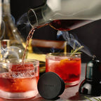 Cocktail being poured with smoke effect into a glass on a bar counter.